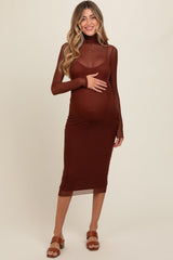 woman wearing a brown long sleeve maternity dress with a sheer top layer and baby bump visible