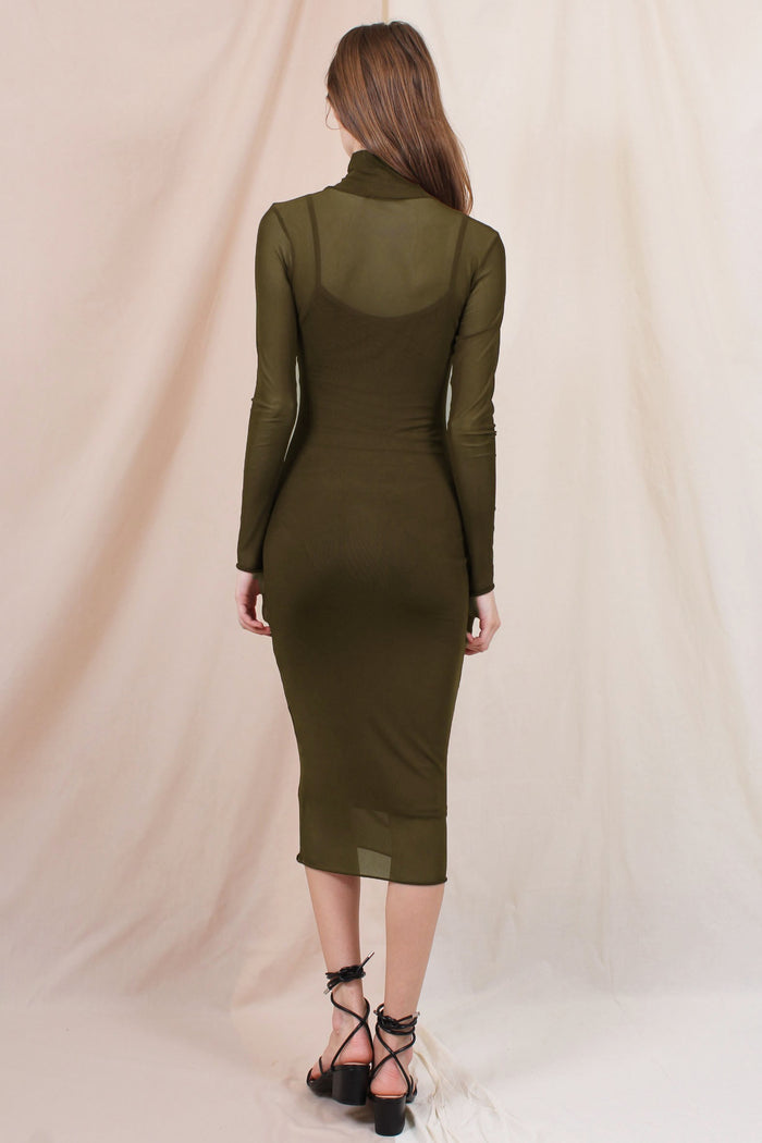woman wearing a fitted olive green long sleeve midi dress with a sheer overlay and a mock neck