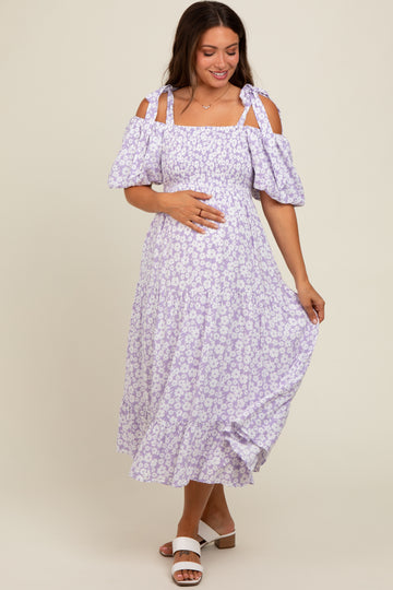 woman wearing a purple floral maternity dress with off-the-shoulder sleeves and holding her baby bump