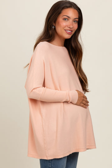 woman wearing a light peach oversized maternity top and holding her baby bump