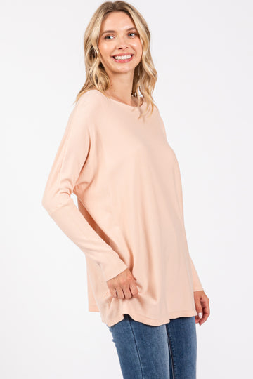 woman wearing a light peach long sleeve top with a relaxed fit and side slits, paired with blue jeans