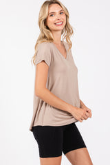 woman wearing a beige short sleeve v-neck top and black bike shorts, smiling and standing sideways