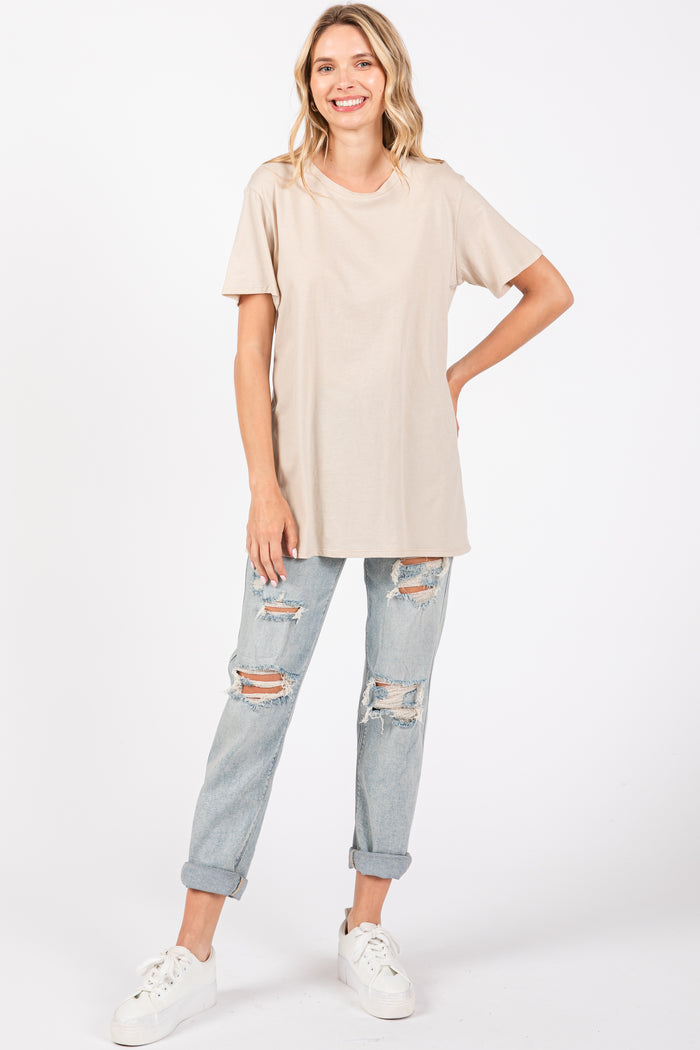 woman wearing a beige oversized t-shirt and distressed light blue jeans, smiling with hands on hips
