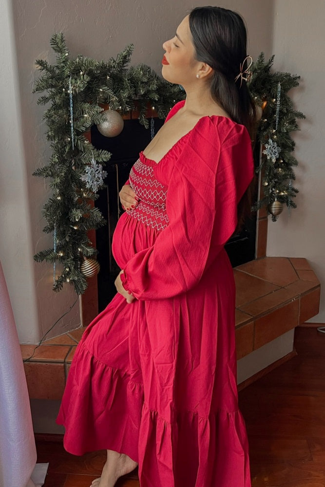 woman wearing a bright pink maternity dress with gathered bodice and long sleeves, cradling her baby bump