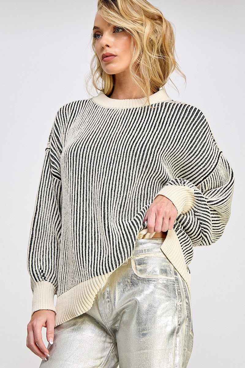 woman wearing a black and cream striped oversized sweater with balloon sleeves and side slits, paired with shiny silver pants