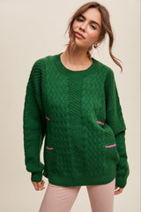woman wearing a green cable knit sweater with contrasting pink detailing on the front