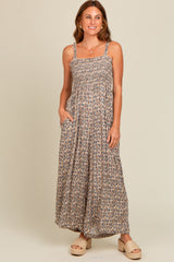 woman wearing a brown floral maxi dress with adjustable straps and pockets, standing and smiling