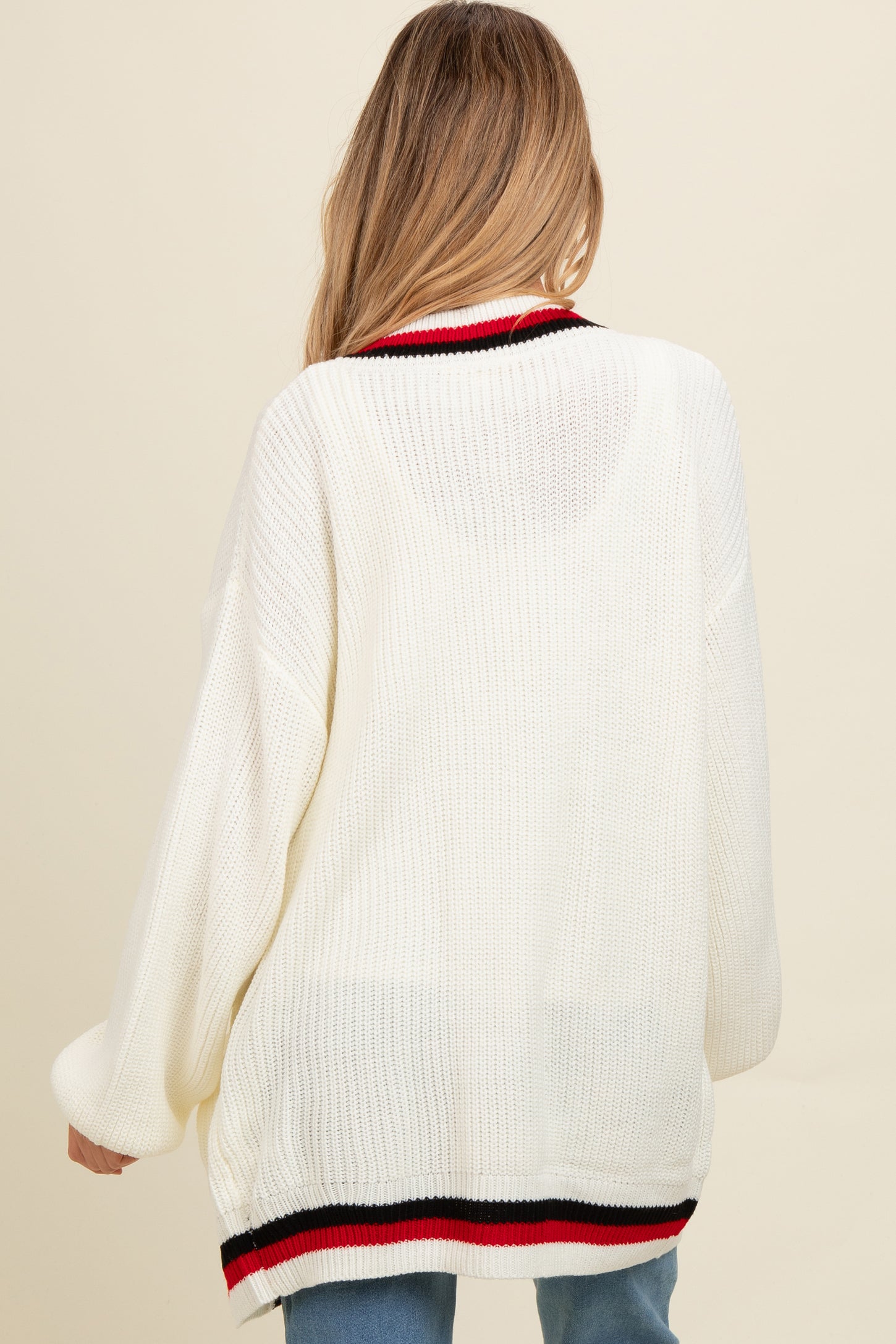 woman wearing a loose-fitting cream maternity sweater with black and red striped details on the hem