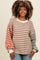 woman wearing a striped oversized sweatshirt in brown, red, and green tones paired with light blue jeans