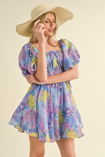woman wearing a purple floral puff sleeve mini dress and a wide-brimmed straw hat