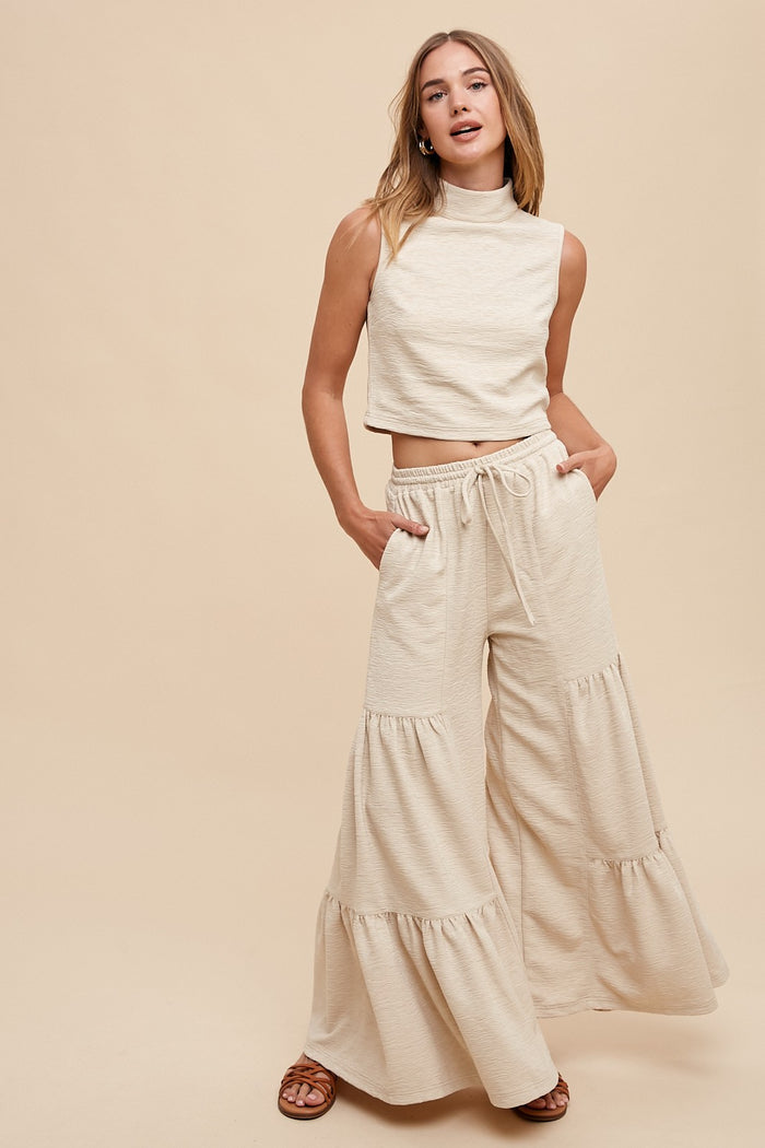 woman wearing a cream sleeveless crop top and wide-leg tiered pants with pockets