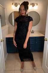 woman wearing a black lace midi dress with short sleeves and a fitted silhouette, standing in a bathroom