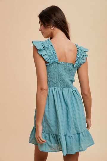 woman wearing a teal shirred back mini dress with ruffle sleeves and a tiered skirt