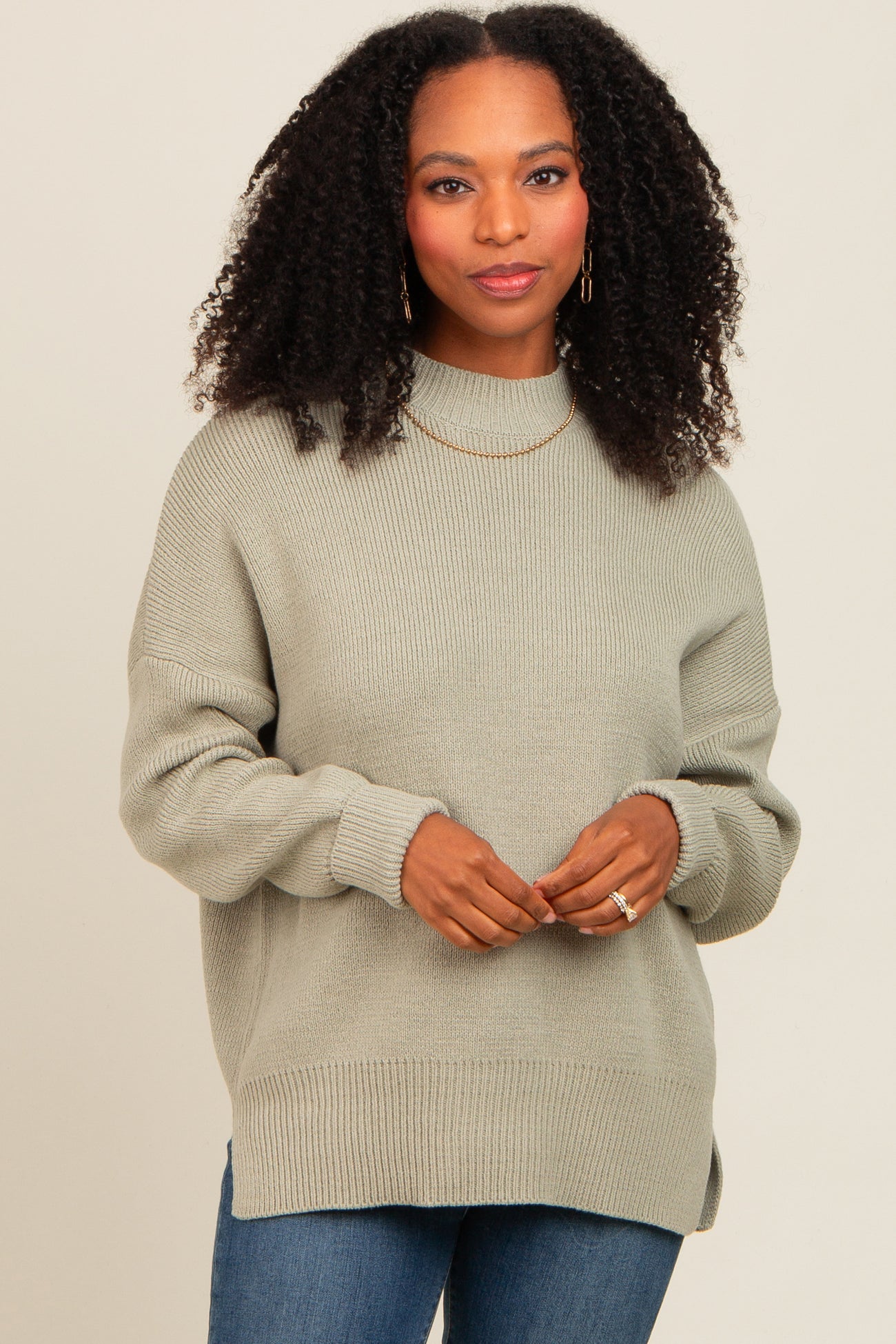 woman wearing a light green oversized knit sweater with a high neckline and side slits, paired with jeans