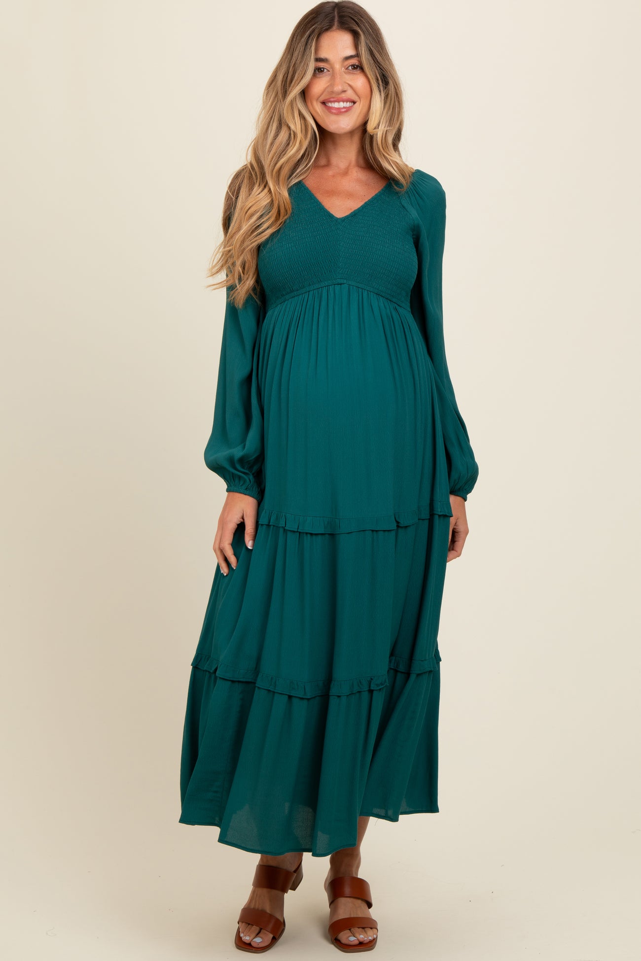 woman wearing a teal maternity maxi dress with long sleeves and tiered layers, showcasing her baby bump