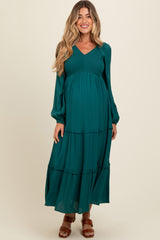 woman wearing a teal maternity maxi dress with long sleeves and tiered layers, showcasing her baby bump