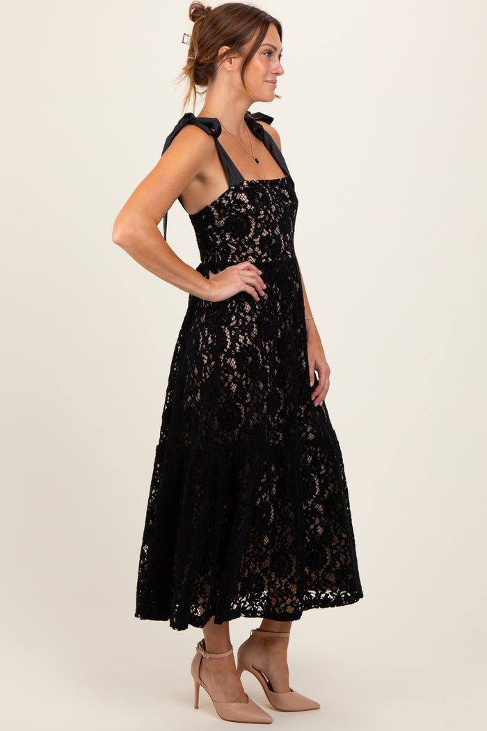 woman wearing a black lace midi dress with bow tie straps and nude heels, posing in profile