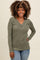 woman wearing a green ribbed long sleeve top with a v-neck and button details, smiling at the camera