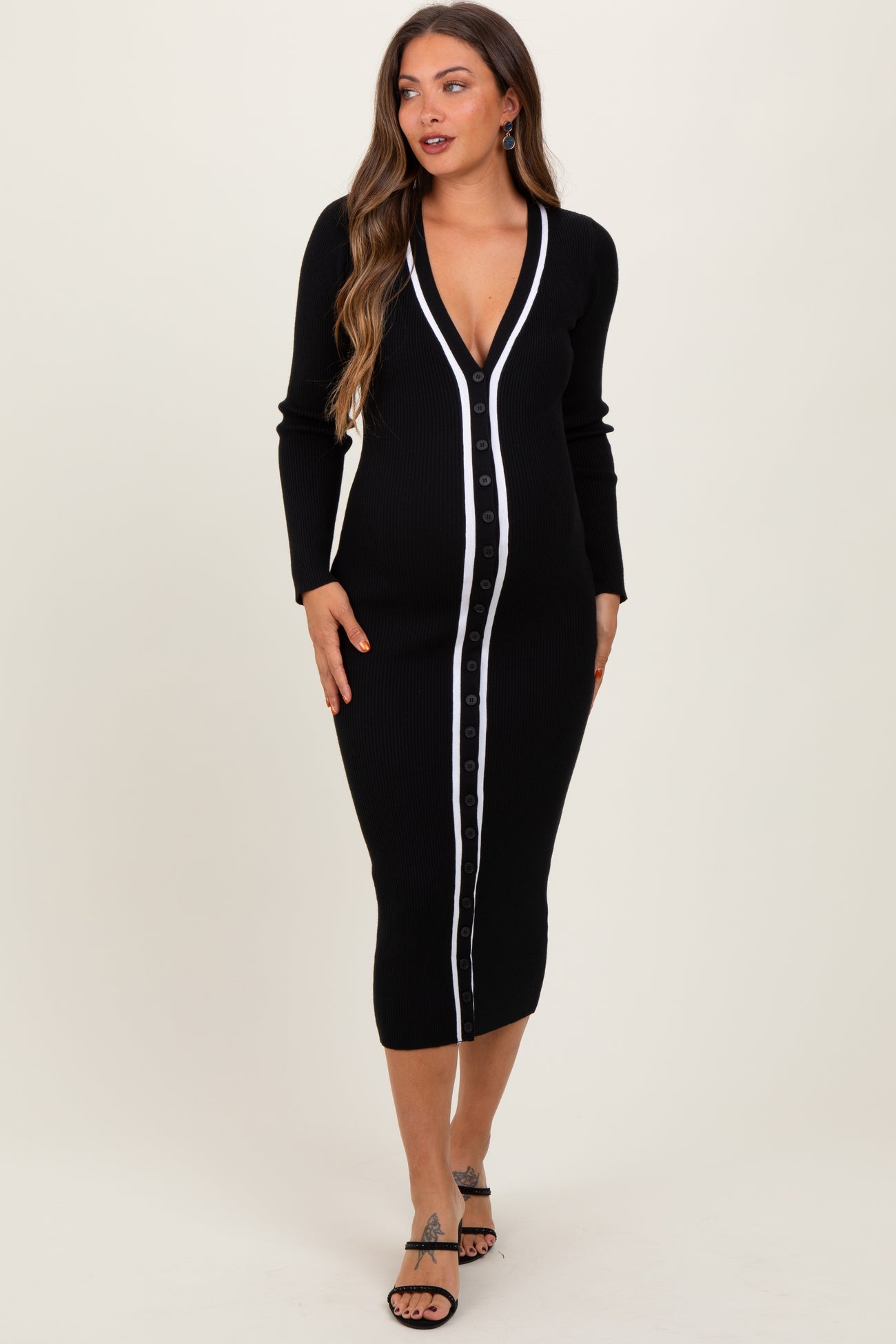 woman wearing a black maternity dress with a button-down front and white stripe detailing, posing with a baby bump visible
