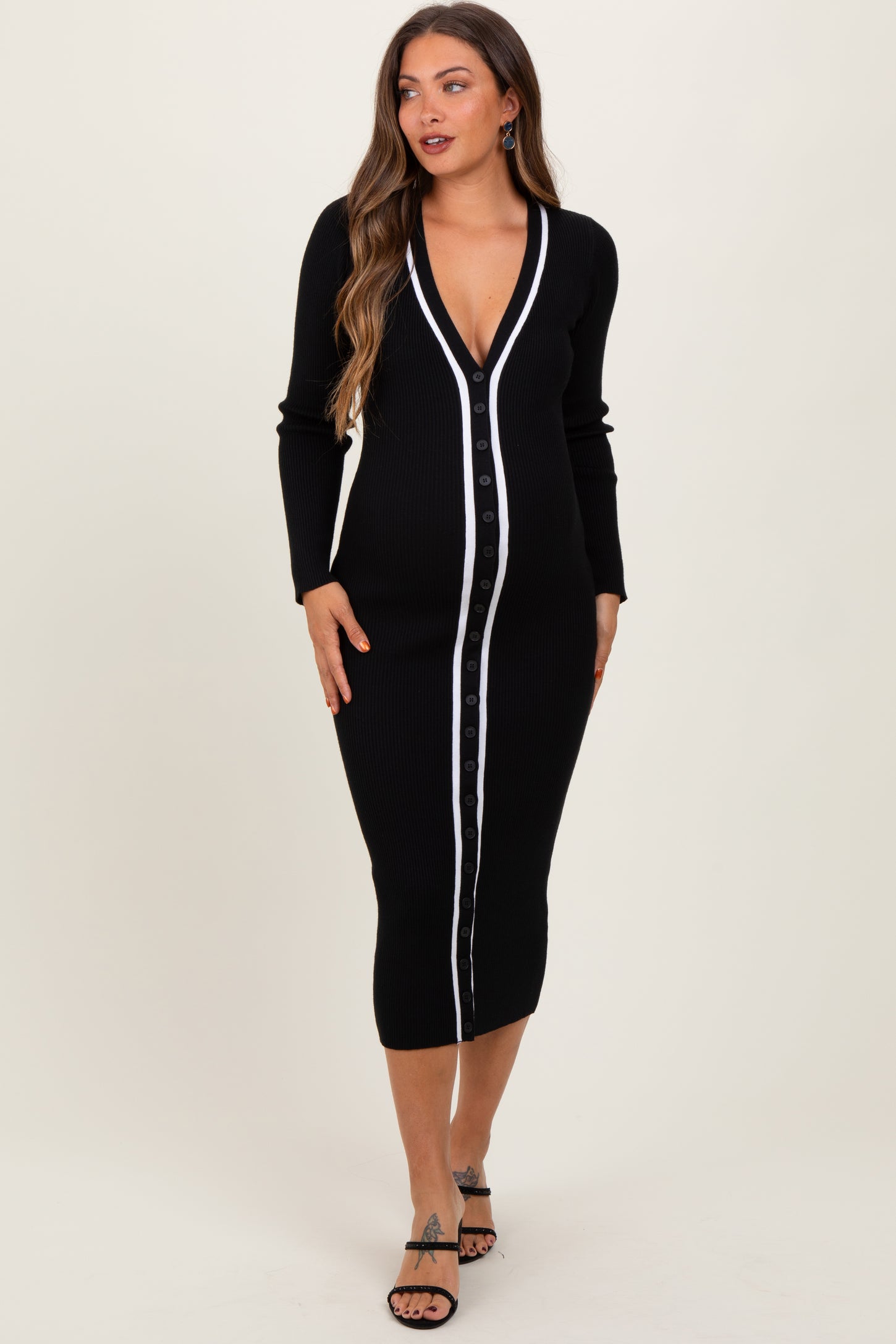 woman wearing a black maternity dress with a button-down front and white stripe detailing, posing with a baby bump visible