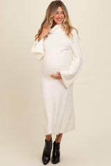 woman wearing a cream long sleeve maternity dress with a cowl neck, holding her baby bump