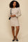 woman wearing a beige cable knit sweater dress with ruffle hem and long sleeves, styled with black flats and a handbag