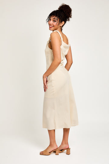 woman wearing a beige sleeveless midi dress with a relaxed fit and ruffled straps, standing against a light background