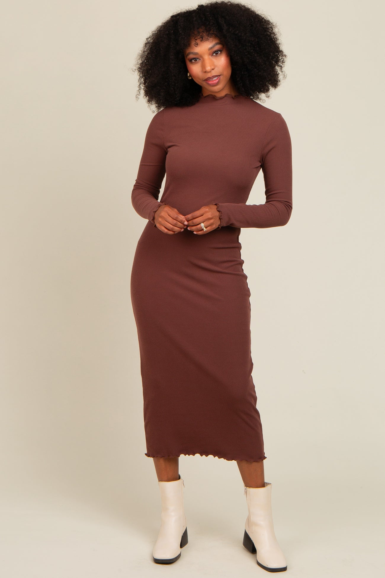 woman wearing a brown ribbed long sleeve midi dress with a scalloped hem and standing in front of a neutral background