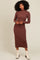 woman wearing a brown ribbed long sleeve midi dress with a scalloped hem and standing in front of a neutral background