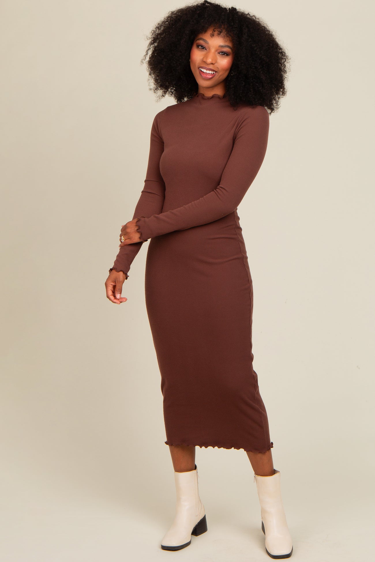 woman wearing a brown long sleeve ribbed midi dress and white ankle boots, smiling with hands on her hips