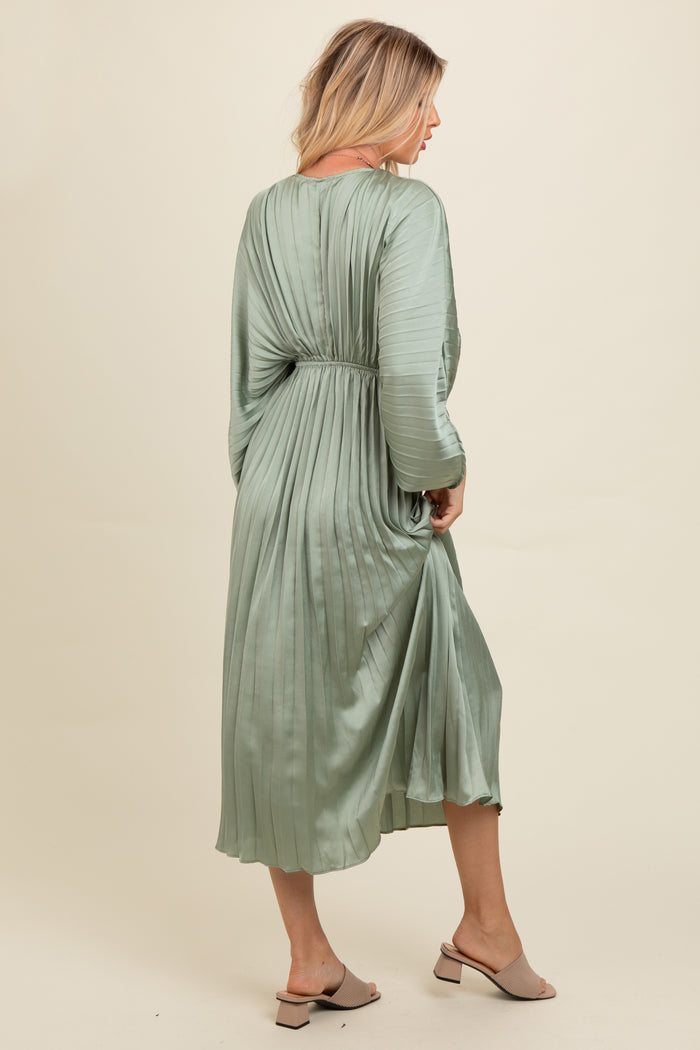 woman wearing a green pleated midi dress with long sleeves and a cinched waist, standing sideways