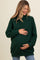 woman wearing a dark green maternity turtleneck sweater and holding her baby bump