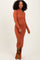 woman wearing a rust ribbed midi dress with long sleeves and a fitted silhouette, posing with a smile