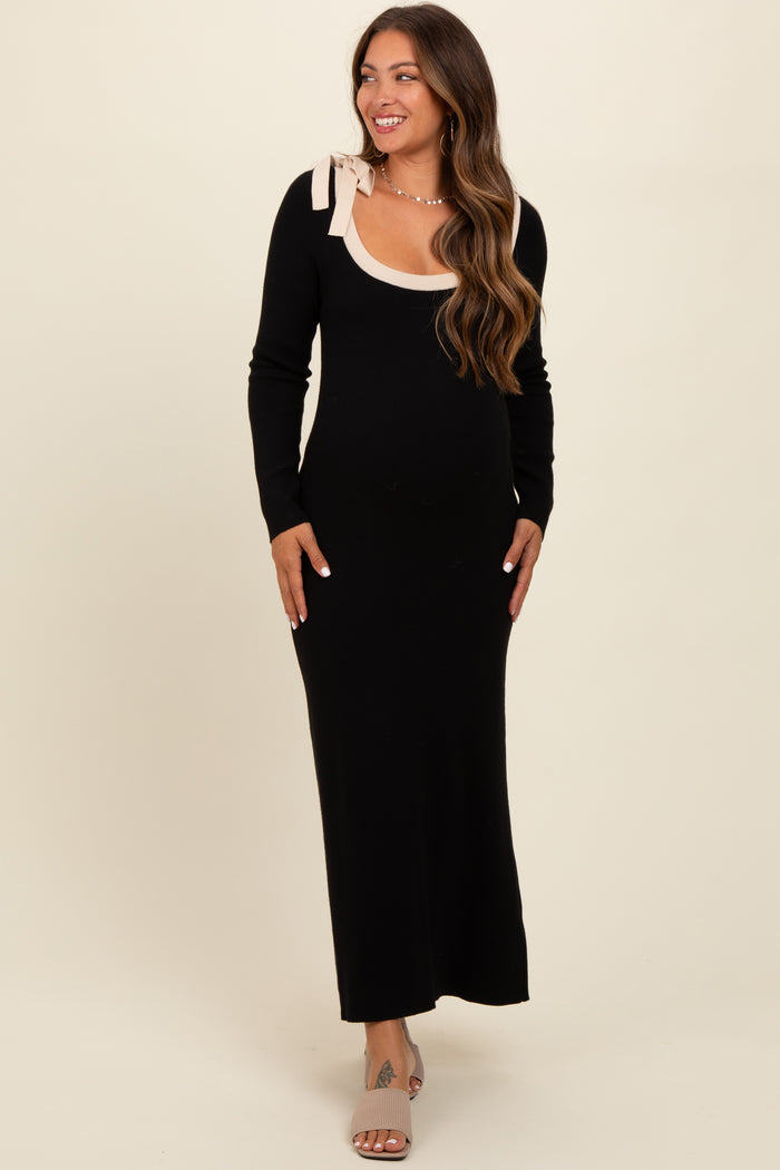 woman wearing a black long sleeve maternity dress with a scooped neckline and a bow detail on the shoulder, showing her baby bump