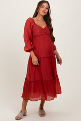 woman wearing a red tiered maternity dress with long puff sleeves and a sweetheart neckline, showing her baby bump