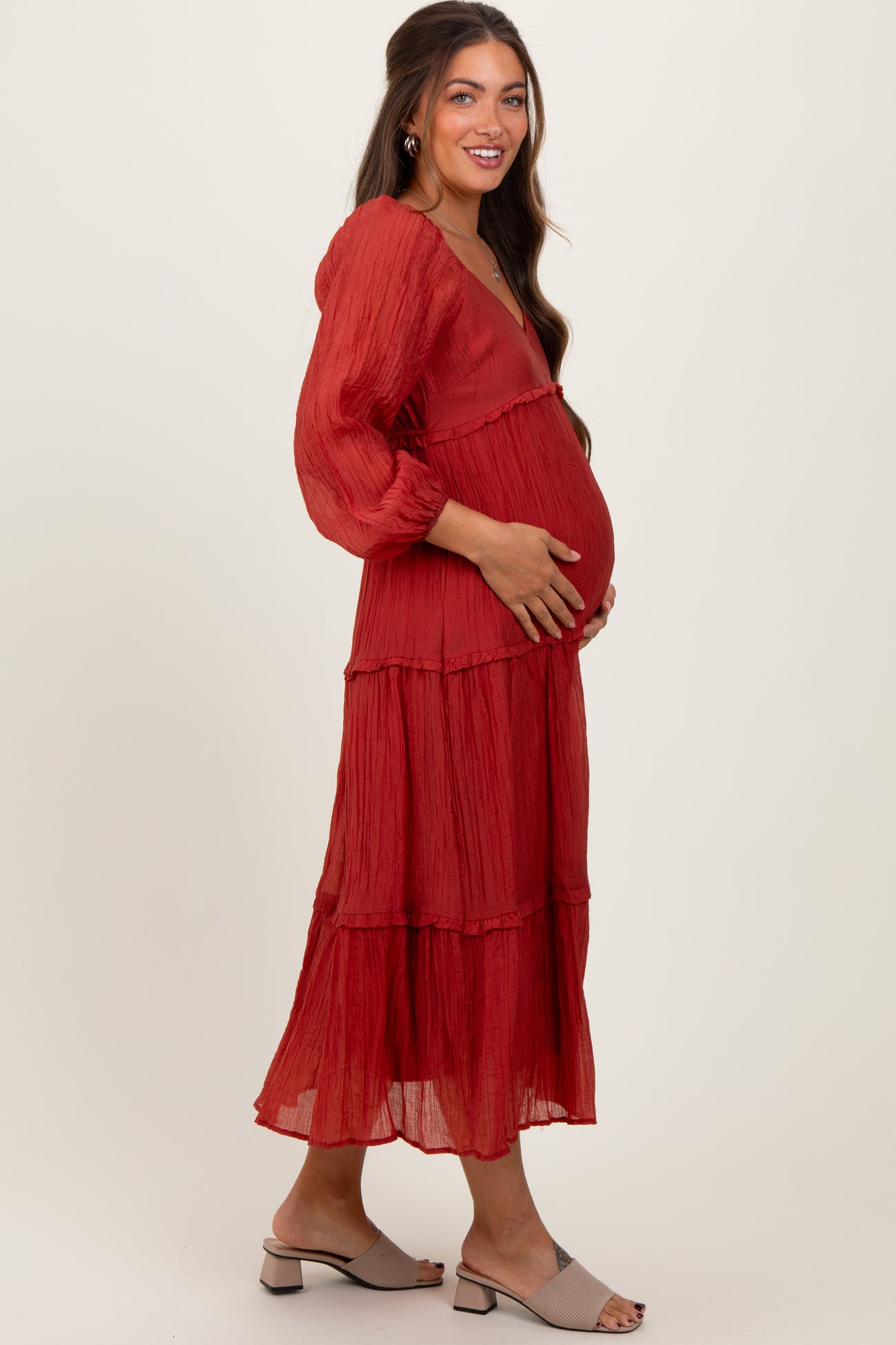 woman wearing a red tiered maternity maxi dress, cradling her baby bump, with long sleeves and a v-neckline