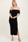 woman wearing a black off-the-shoulder midi dress with a bow detail and side slit, standing with hands on her hips