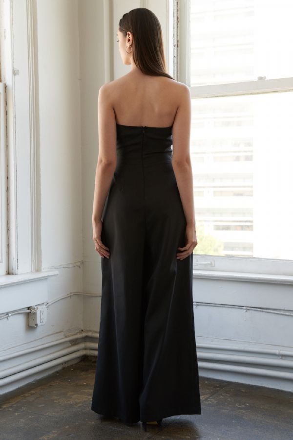 woman wearing a black strapless jumpsuit, seen from the back, with a fitted bodice and wide-leg trousers
