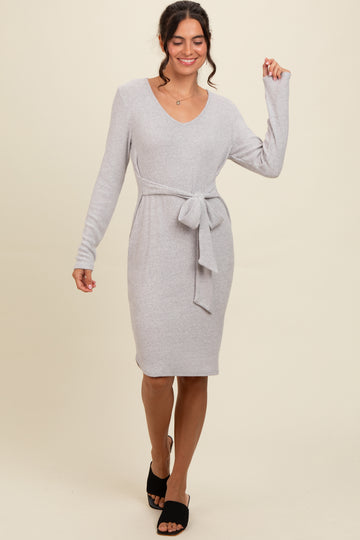 woman wearing a light gray ribbed sweater dress with a belted waist and long sleeves, posing confidently