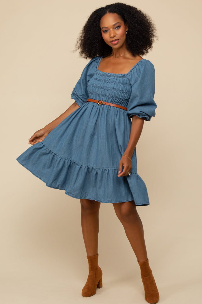 woman wearing a denim smocked square neck dress with a ruffled hem and a tan belt, styled with brown ankle boots