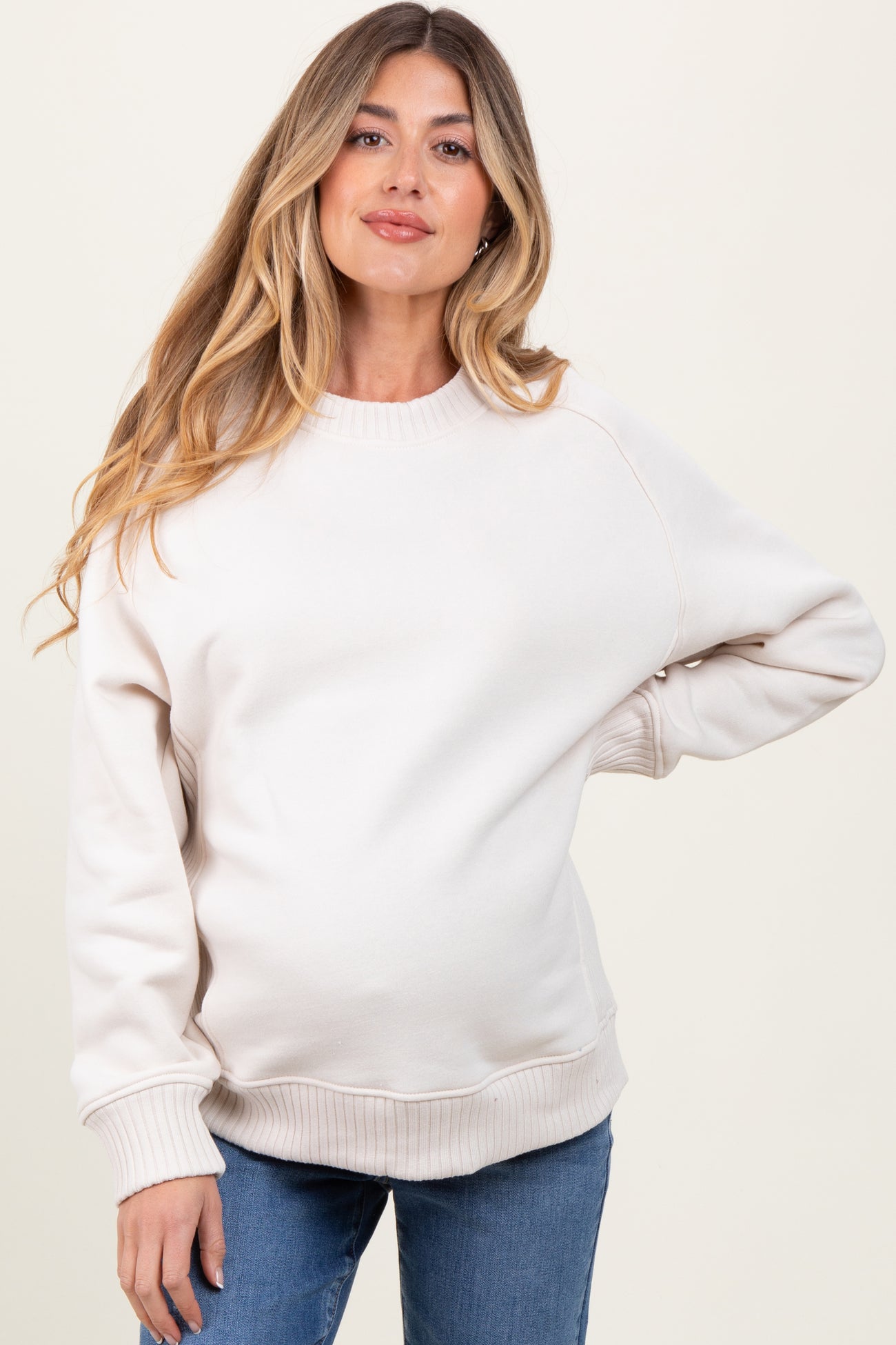 woman wearing a beige maternity sweatshirt with a relaxed fit and visible baby bump, styled with blue jeans
