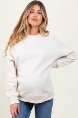 woman wearing a beige maternity sweatshirt with a relaxed fit and visible baby bump, styled with blue jeans