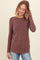 woman wearing a maroon long sleeve ribbed top and smiling with one hand in her hair