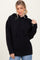 woman wearing a black oversized hooded sweater with a front pocket and ribbed cuffs, styled with light blue jeans