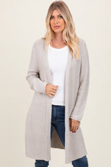 woman wearing a light grey long sleeve open front cardigan over a white top and blue jeans