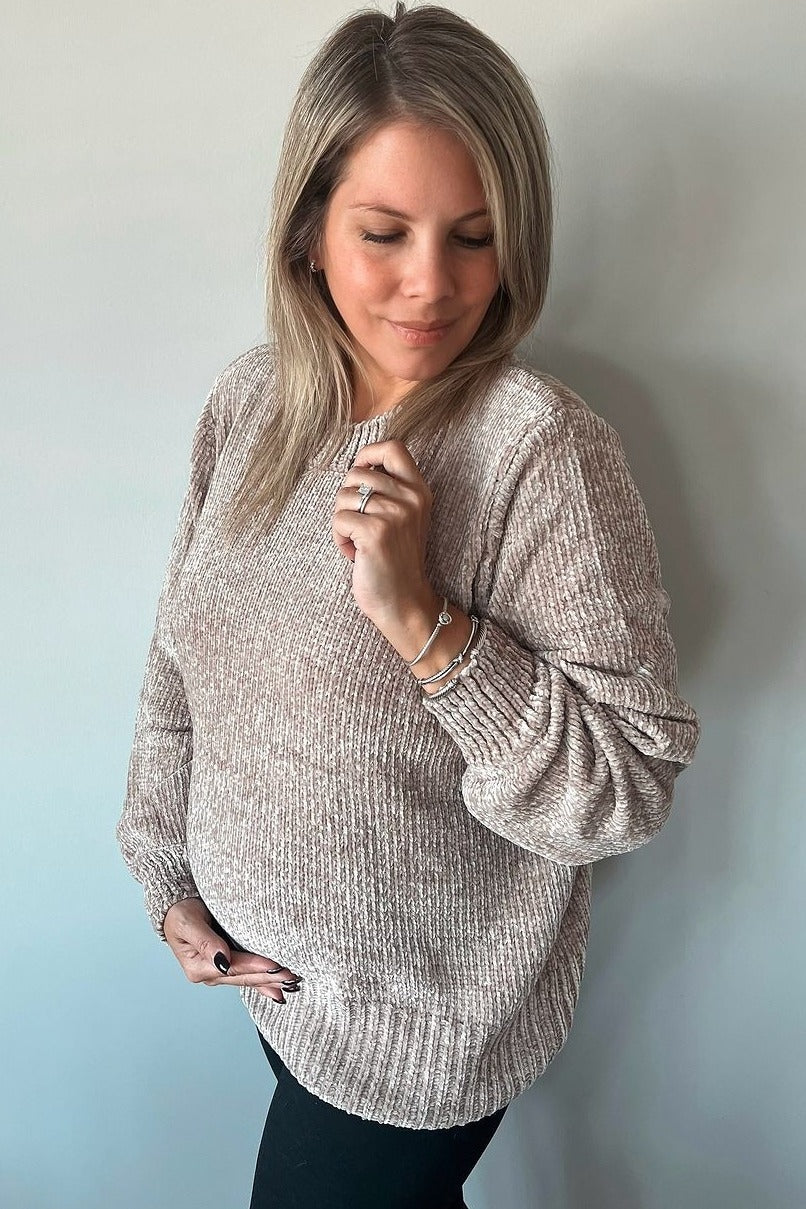woman wearing a light beige maternity sweater with textured fabric, resting her hand on her baby bump