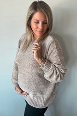 woman wearing a light beige maternity sweater with textured fabric, resting her hand on her baby bump