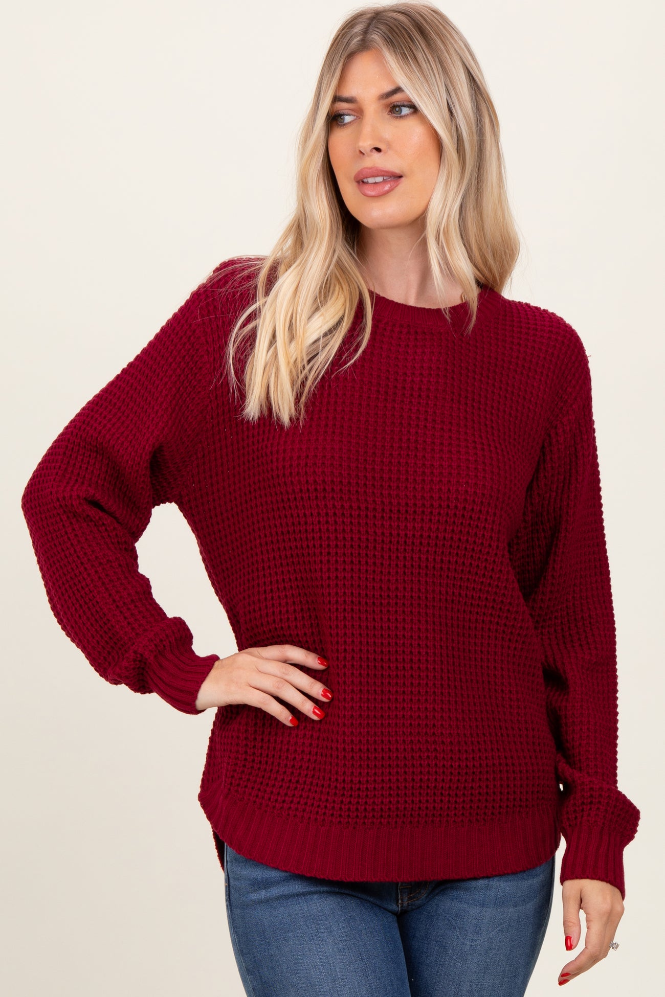 woman wearing a burgundy knit sweater with long sleeves and a relaxed fit, paired with blue jeans