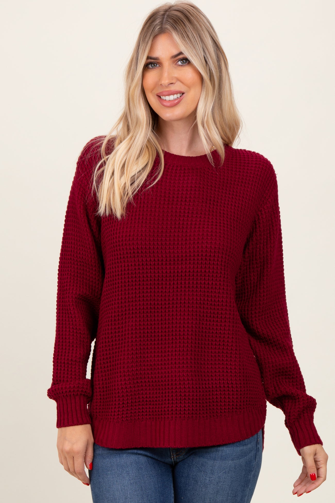 woman wearing a burgundy knit sweater with a textured design and relaxed fit, paired with blue jeans