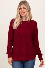 woman wearing a burgundy knit sweater with a textured design and relaxed fit, paired with blue jeans